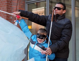 Der blinde Mobilitätstrainer Juan Ruiz trainiert mit einem Kind Klicksonar, sie haben durch Klicken und den Einsatz ihrer Langstöcke eine Eisskulptur entdeckt